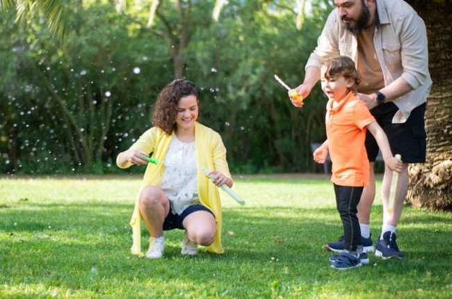 A family enjoys a playful day with bubbles in a sunny park setting.