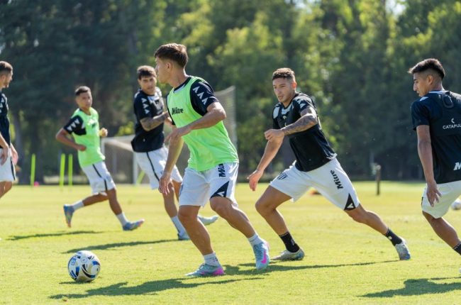 Teenage soccer players in team jerseys practice on a sunny outdoor field.