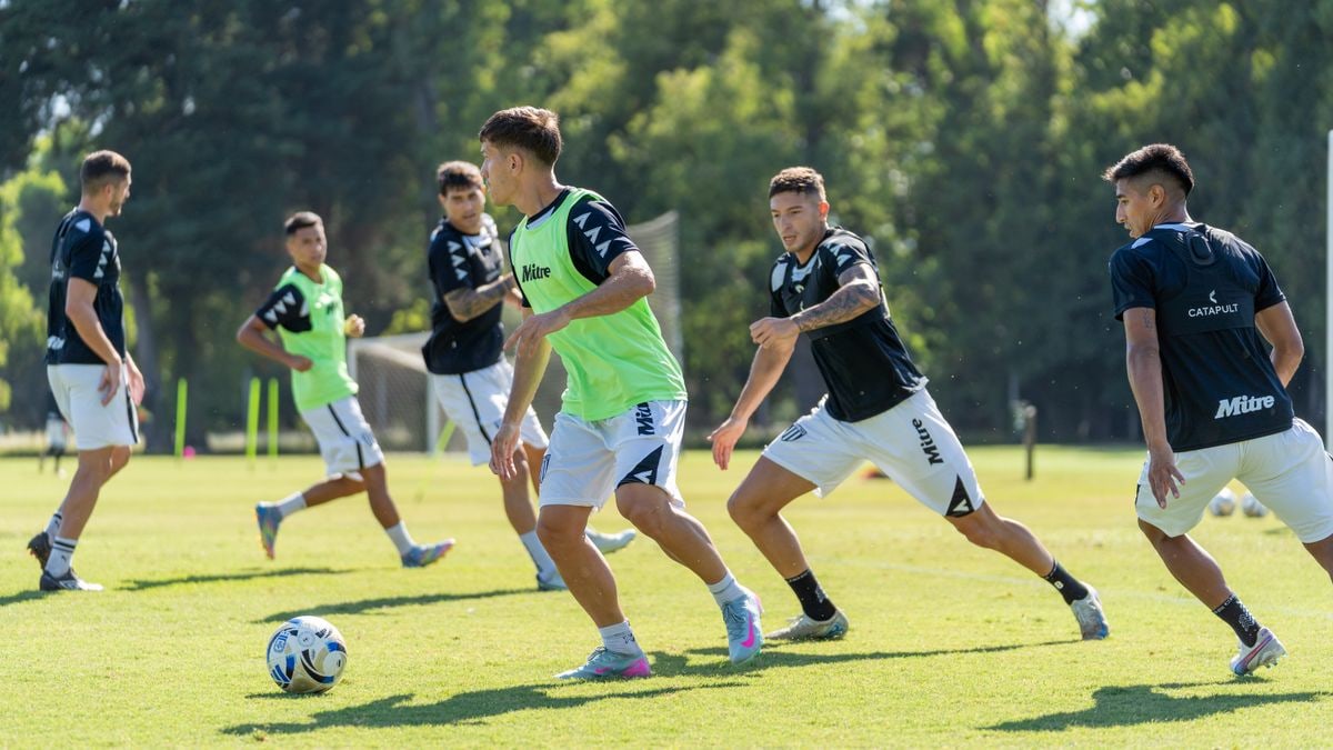 Teenage soccer players in team jerseys practice on a sunny outdoor field.